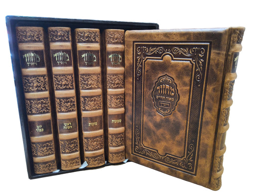 A set of ornate, antique-style leather-bound books displayed in a black presentation box on a wooden table, with bookshelves visible in the background.