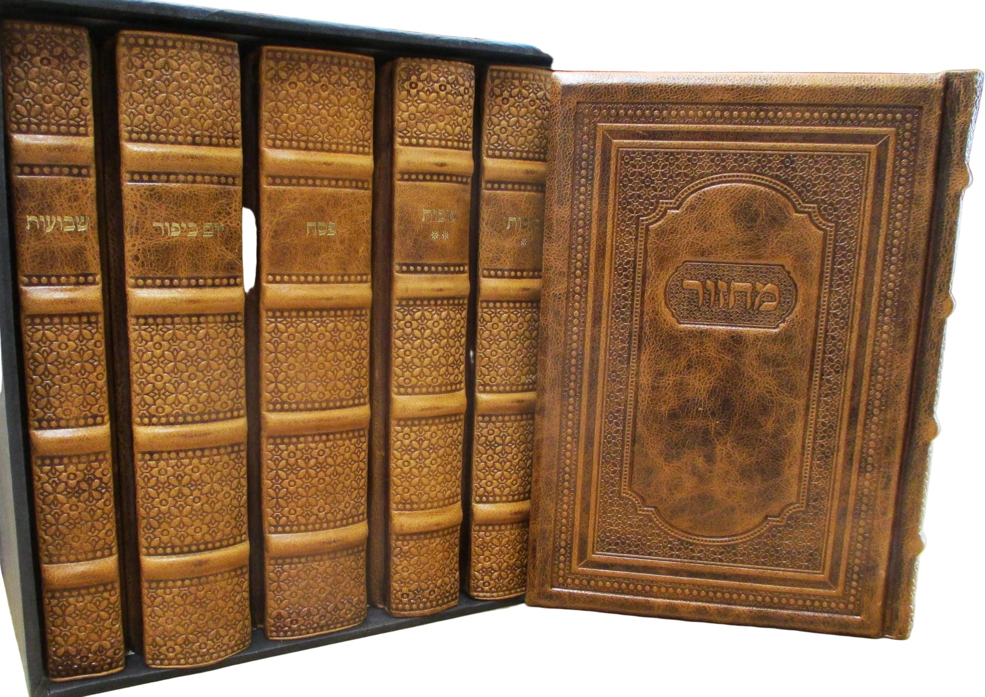 A set of five ornate brown leather-bound books with gold Hebrew lettering on the spines, displayed in a black presentation box with the front cover open to show the title page, set on a light wood tabletop.